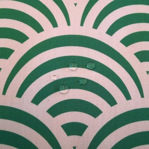 May include: A close-up of a white fabric with a green geometric pattern. Several water droplets are scattered across the fabric.