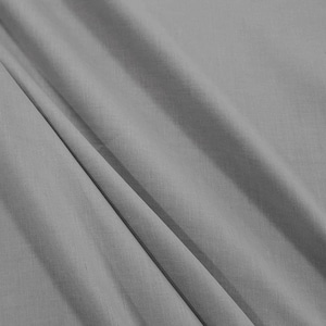 May include: A close-up of a smooth, gray fabric with a subtle texture. The fabric is folded and draped, creating soft folds and wrinkles.