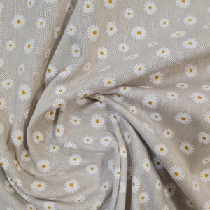 May include: A beige fabric with a white daisy pattern. The fabric is textured and has a subtle sheen.