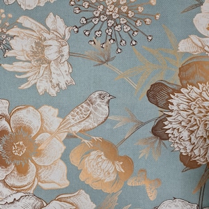 Könnte beinhalten: Nahaufnahme eines Tapetendesigns mit Vogel- und Blumenmuster. Die Tapete hat einen hellblauen Hintergrund mit goldenen und weißen botanischen Illustrationen. Das Design umfasst Blumen, Blätter und einen Schmetterling.