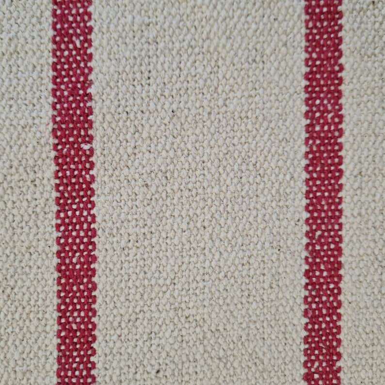 Puede incluir: Primer plano de una tela blanca con dos rayas rojas que corren verticalmente por el centro. La tela tiene una textura tejida.
