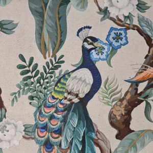 Pu&ograve; includere: Un pavone colorato con piume blu, verdi e bianche &egrave; raffigurato su uno sfondo beige con foglie verdi e fiori bianchi. Le piume della coda del pavone sono disposte a ventaglio.