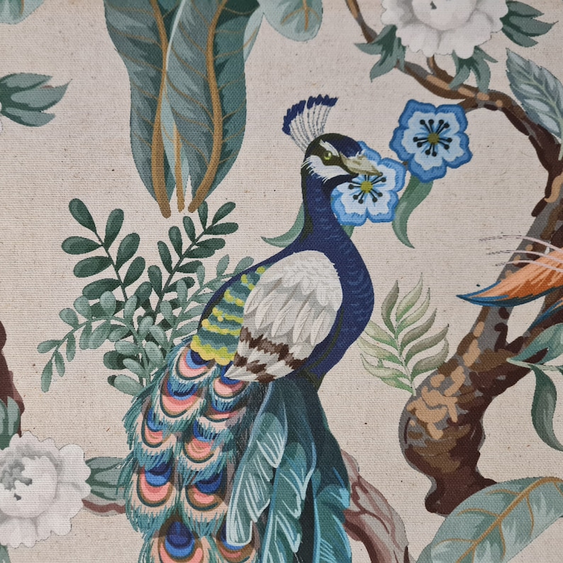 Pu&ograve; includere: Un pavone colorato con piume blu, verdi e bianche &egrave; raffigurato su uno sfondo beige con foglie verdi e fiori bianchi. Le piume della coda del pavone sono disposte a ventaglio.