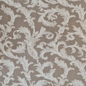 Può includere: Primo piano di un tessuto con un motivo ripetuto di disegni floreali e di foglie bianche stilizzate su uno sfondo marrone. Il motivo ha un'estetica vintage e ornata, adatta per tappezzeria o scopi decorativi.