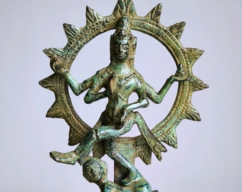 May include: A bronze statue of a deity with multiple arms, surrounded by a sun-like halo. The figure is in a dynamic pose, with one leg raised and a smaller figure at the base. The statue has a weathered, antique appearance.