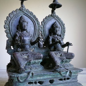 May include: A pair of bronze statues of deities seated on a throne, with intricate details and a green patina. The statues are adorned with jewelry and elaborate headdresses.