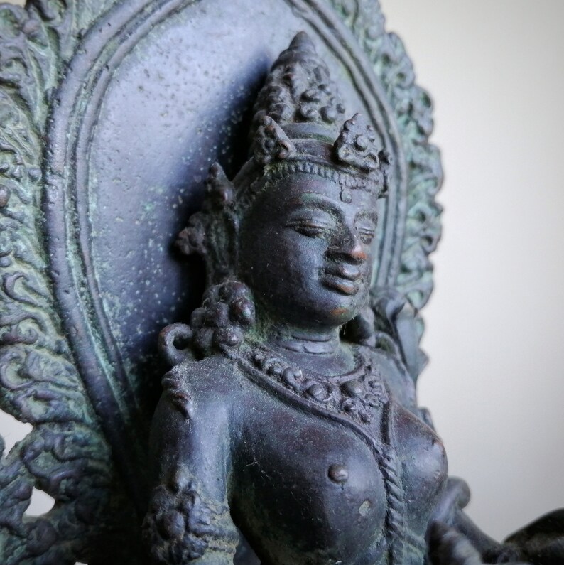 May include: A dark bronze statue of a deity seated on a throne with a decorative back. The deity has a crown and intricate jewelry. The statue is detailed and has a weathered finish.