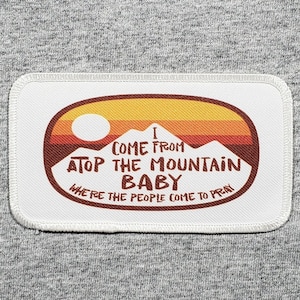 May include: White patch with a red, orange, and yellow sunset graphic and the text "I come from atop the mountain baby where the people come to pray".