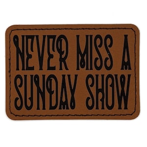 May include: A rectangular brown leather patch with the phrase "NEVER MISS A SUNDAY SHOW" in bold, black, stylized lettering. The patch has a stitched border and a vintage aesthetic.