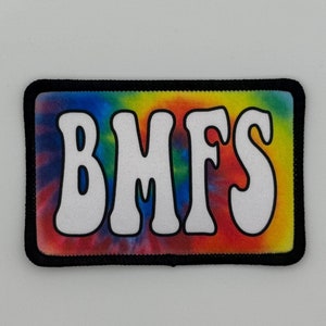 May include: Rectangular patch with a tie-dye background in shades of blue, green, yellow, and red. The patch has a black border and the white letters "BMFS" in a bold, rounded font.