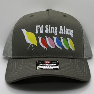 May include: A gray trucker hat with a white mesh back. The front of the hat has a white graphic of a line of colorful birds with the text "I'd Sing Along". The hat has a black label with the text "Richardson" and "Original 112 Trucker Adjustable".