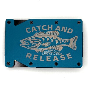 May include: A teal metal wallet with the words "CATCH AND RELEASE" and a fish graphic engraved on the front. The text "ONLY BREAK ONE LAW AT A TIME" is below the fish. The wallet has black screws.
