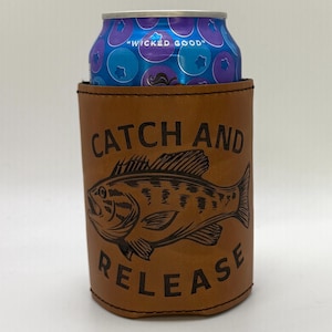 May include: A brown leather can cooler with the words "CATCH AND RELEASE" and a fish graphic. The can cooler holds a blue and purple can with the text "WICKED GOOD".