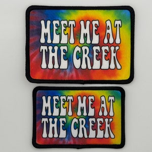 May include: Two tie-dye patches with black borders. The patches are rectangular and feature the text "Meet Me At The Creek" in white, outlined in black. The patches are different sizes.
