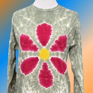 May include: A long-sleeved shirt with a tie-dye pattern in shades of green, white, and pink. A large pink flower with a yellow center is centered on the shirt.