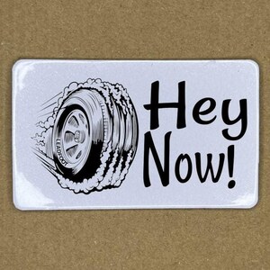 May include: A white sticker with a black and white illustration of a tire with smoke coming from it. The text "Hey Now!" is written in black below the tire.