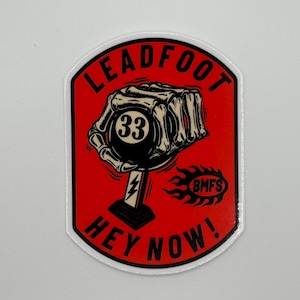 May include: A red and white sticker with a skeleton hand holding a black and white billiard ball with the number 33 on it. The sticker says "Leadfoot Hey Now!" and has a small flame with the text "BMFS" on it.