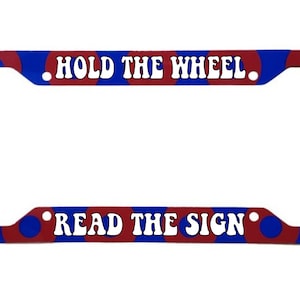 May include: Red and blue license plate frame with white text that reads "Hold the Wheel Read the Sign".