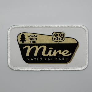 May include: White embroidered patch with a black and gold design. The design features a stylized tree, the text "Away from the", the number "33" in a circle, the word "Mine", and the text "National Park".