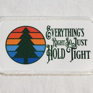May include: White rectangular patch with a green pine tree silhouette in a circle with a sunset design. The text "Everything's Right So Just Hold Tight" is written in green cursive.