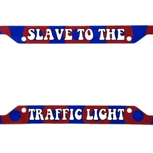 May include: Red and blue license plate frame with the text "SLAVE TO THE TRAFFIC LIGHT" in white.