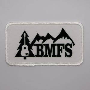 May include: White embroidered patch with a black silhouette of a mountain range, a pine tree with a guitar, and the text "BMFS".