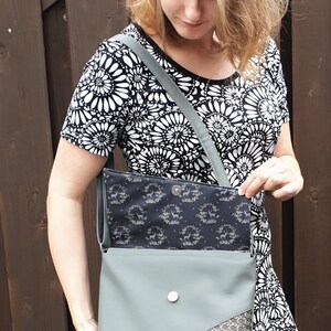 Puede incluir: Bolso bandolera verde salvia con solapa estampada y esquina decorativa. El bolso tiene un cierre plateado y una correa a juego. El forro interior presenta un estampado floral azul oscuro.