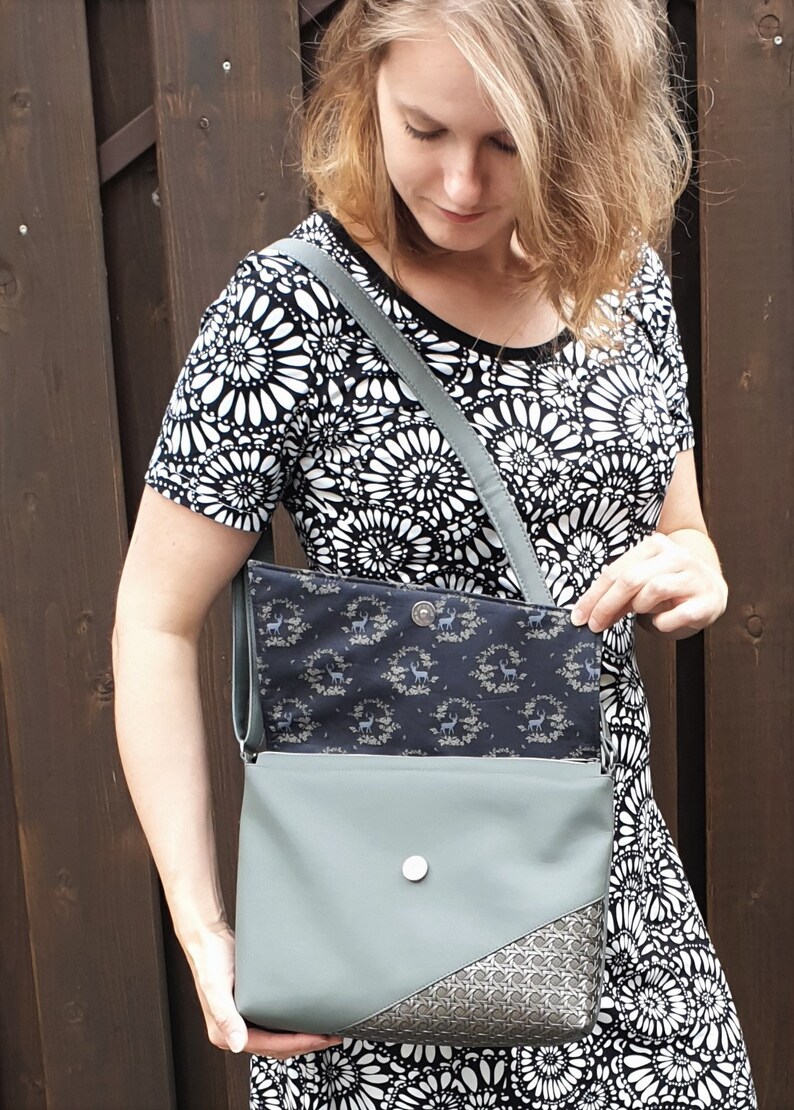 Puede incluir: Bolso bandolera verde salvia con solapa estampada y esquina decorativa. El bolso tiene un cierre plateado y una correa a juego. El forro interior presenta un estampado floral azul oscuro.