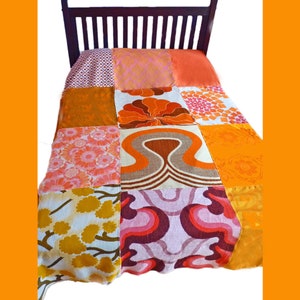 May include: A patchwork quilt featuring a range of orange, pink and brown floral designs. The quilt is made from various fabrics and stitched together in a grid pattern.