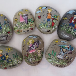 May include: Hand-painted decorative stones featuring children with backpacks and the names Richard, Noa, Linus, Henri, Jesse, Hanna, and Matilda. Each stone has a unique design with flowers, suns, and insects.