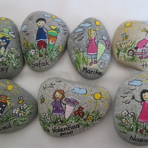 May include: Hand-painted decorative stones featuring children with school cones, flowers, and sunny skies. Each stone has a child's name, such as Kuzey, Safak, and Marika. The artwork includes details like bees, birds, and a bicycle.