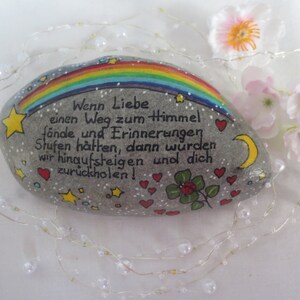 May include: A smooth gray river stone painted with a colorful rainbow, yellow stars, a yellow crescent moon, red hearts, and a green four-leaf clover. The German text reads: Wenn Liebe einen Weg zum Himmel f&auml;nde und Erinnerungen Stufen h&auml;tten, dann w&uuml;rden wir hinaufsteigen und dich zur&uuml;ckholen!