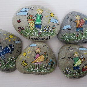 May include: Hand-painted rocks featuring children with school cones, suns, clouds, and flowers. Each rock has a child's name: Leonhardt, Timo, Marie, Sophie Marie, and Hendrik. The artwork is colorful and whimsical, with a cheerful, childlike style.