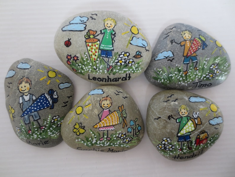 May include: Hand-painted rocks featuring children with school cones, suns, clouds, and flowers. Each rock has a child's name: Leonhardt, Timo, Marie, Sophie Marie, and Hendrik. The artwork is colorful and whimsical, with a cheerful, childlike style.