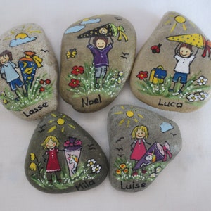 May include: Five hand-painted stones with illustrations of children, school cones, and flowers. Each stone features a child's name: Lasse, Noel, Luca, Mila, and Luise. The artwork includes a sun, clouds, and a ladybug.