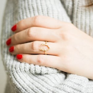 Könnte beinhalten: Ein goldener Ring mit einem zarten, gedrehten Design. Der Ring wird am Finger einer Hand mit rotem Nagellack getragen.
