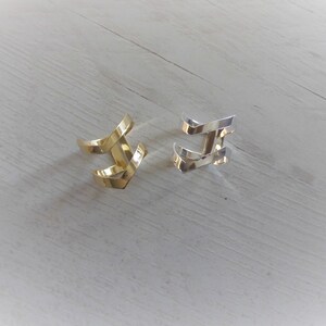 May include: Two ear cuffs, one gold and one silver, in a simple geometric design. The cuffs are made of metal and have a slightly curved shape.