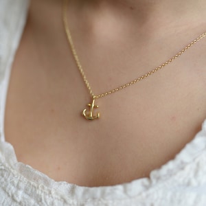 Może przedstawiać: Delikatny złoty naszyjnik z małym zawieszką w kształcie kotwicy.