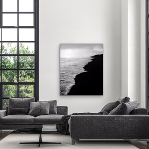 May include: Black and white photograph of a beach with waves crashing on the shore. The water is on the left side of the image and the sand is on the right side.