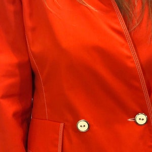 May include: A bright red blazer with white stitching and two gold buttons. The blazer has a pocket on the left side.