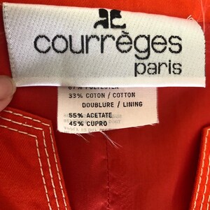 May include: A white tag with black text that reads "courr&egrave;ges paris". The tag is attached to a red fabric garment. The tag also includes the following information: 67% Polyester, 33% Cotton, Doublure/Lining 55% Acetate, 45% Cupro.