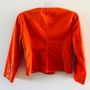 May include: A bright orange blazer with long sleeves and white stitching. The blazer has a single button on each cuff and a single button on the back.