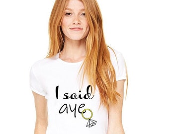 Könnte beinhalten: Weißes T-Shirt mit schwarzem Text, der "I said aye" lautet, und einem schwarzen und gelben Ring mit einem Diamanten.