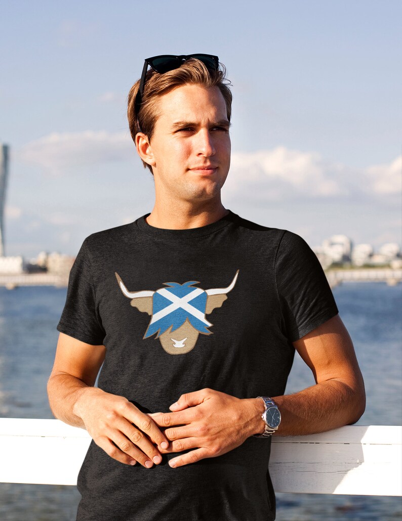 May include: A dark grey t-shirt with a brown highland cow graphic. The cow's face is replaced with the Scottish flag.