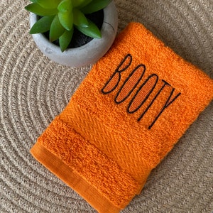 May include: Orange hand towel with the word "BOOTY" embroidered in black thread.