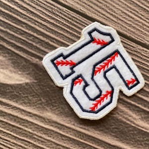 May include: White felt patch with a navy blue outline of the letters "SF" with red stitching resembling baseball seams.