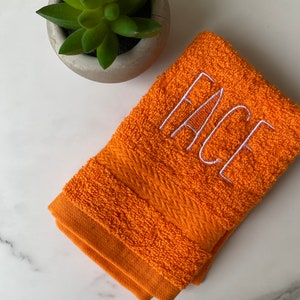 May include: Orange hand towel with white embroidered text that reads "FACE".