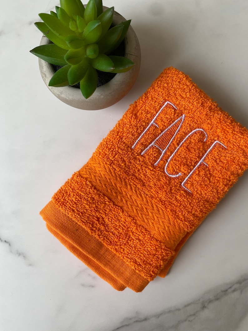 May include: Orange hand towel with white embroidered text that reads "FACE".