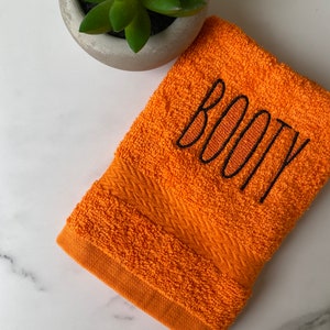 May include: Orange hand towel with black embroidered text that says "BOOTY".