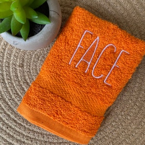 May include: Orange hand towel with the word "FACE" embroidered in white.